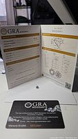 GRA Moissanite grading report booklet opened to show grading results alongside loose moissanite and warranty card