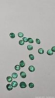 Close-up image showing multiple natural round cut emeralds scattered on white surface, displaying rich green color and clarity.