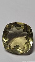 Close-up photo of natural lemon citrine, cushion cut gemstone with light yellow-green hue, good clarity, faceting visible