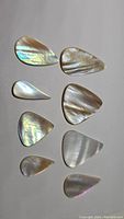 Eight pear-shaped natural mother of pearl cabochons laid out in a flat arrangement on a plain background, showing varied sizes and rainbow-like iridescence.