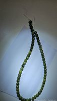 Full view of the green jade bead strand showing beads in various shades of green on a white background.