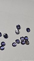 Photo showing 13 small round cabochon iolite loose gemstones with polished, smooth surfaces and violet-blue hues on a plain background.