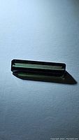 Full view photo of the green tourmaline gemstone showing its octagon cut and rich green color on white background.