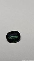 Close-up photo of oval green sapphire gemstone on white background.
