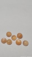 Seven small round peach moonstone cabochons arranged on a neutral surface.