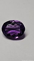 Oval cut purple amethyst gemstone shown from above highlighting deep purple color and internal facets.