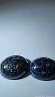 Pair of oval cabochon blue pietersite gemstones side by side showing deep blue color with gold and bronze flecks