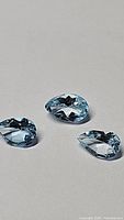 Three pear cut sky blue topaz gemstones displayed on a plain surface showing their clarity and color.