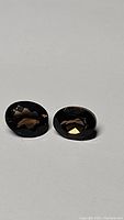 Pair of oval cut smokey quartz gemstones placed on a plain white surface, showing the faceted cuts and dark, smoky brown color.
