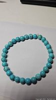 Top-down view of turquoise bead bracelet laid out on white surface showing color and bead uniformity.