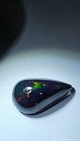 Pear-shaped natural untreated jet black opal with visible flashes of green, red, and yellow colors under light.