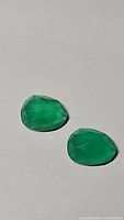 Two vivid green onyx gemstones shown side by side on a light surface, emphasizing color, cut, and clarity.