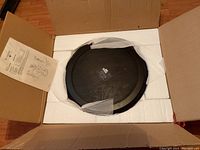 Open box showing one side table top in protective foam packaging, with instruction sheet on the side