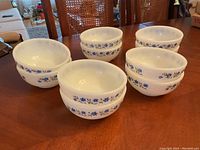 Five white ceramic bowls with blue floral and green vine pattern arranged on table showing pattern and bowl shape.