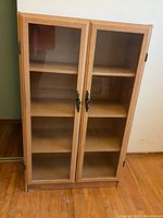 Front view of wooden cabinet with glass doors showing three shelves inside, decorative black metal handles, and water marks at base.