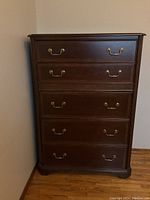Front view of the wooden chest of drawers showing five drawers with brass handles