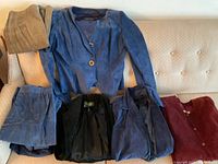 Photo of six clothing items including a blue suede jacket, black suede blazer, blue suede coat, burgundy knit cardigan, and two pairs of suede pants in beige and blue laid out on a sofa.