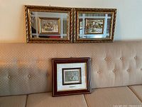 Wide view of all three framed art pieces on couch; two larger gold-tone ornate mirrors with metal relief art, one smaller wood-tone framed metal relief art with matting
