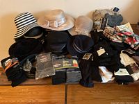 Wide view of hats (black and white striped, beige with bow, black leather, black textured) and many pairs of socks in various packaging and styles spread on table.