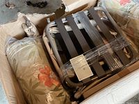 Photo showing a metal frame lawn chair with black straps resting on floral patterned cushions inside an open box.