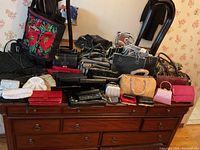 Wide photo showing many small handbags and wallets displayed on a wooden dresser with a mirror in the background.