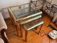 Set of three metal framed nesting tables with glass tops against a wall showing their sizes and condition