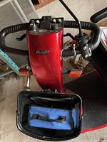 Front view of red tiller with delta handlebar, control panel, headlight and front basket containing blue tool bag.