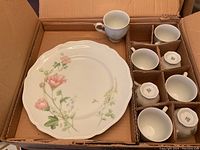 Overview of large dinner plates and matching cups inside open cardboard packaging