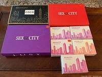 Seven Sex In The City Eau de Parfum boxes alongside three empty gift boxes on wooden surface.