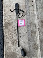 Full view of 1800s cast iron hanging balance beam scale laid on concrete, showing long beam, three hooks, and counterweight.