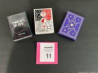 Front view of three distinct playing card decks in their boxes, showcasing unique fantasy-themed packaging designs with text and artwork visible.