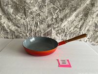 Side view of the orange-red enamel cast iron frying pan with wooden handle on white background.