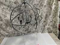 Front view of the modern glass chandelier encased in spiraled chrome metal rings, showing the gyroscope design with glass components inside and hanging crystal chains.