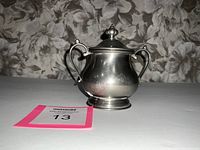 View of the front and two handles of the pewter lidded dish against floral background.