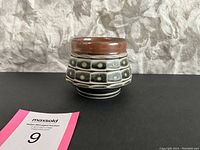 Front and side view of the signed pottery vase showing geometric pattern and brown rim.