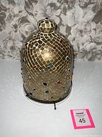 Frontal image of bell-shaped pendant light showing bronze-toned mosaic tiles with colored glass pieces and bronze ring top