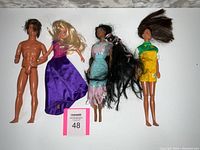 Four older Barbie dolls lying on white surface showing front with dresses and hair detail