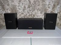 Three-piece set of Pioneer speakers including two bookshelf and one center channel speaker shown with floral curtain background.