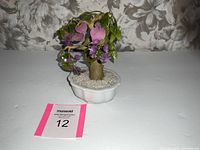 Front view of vintage jade glass bonsai tree with purple flowers in white ceramic pot with pebbles.