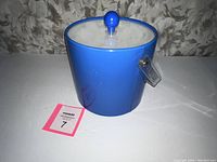 Front view of the blue vinyl ice bucket with clear lid and blue knob on white surface. Shows exterior condition and attached handle.