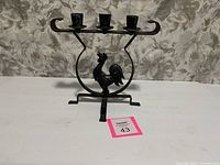 Full frontal image of the metal rooster candlestick holder showing three candle holders and feet support.