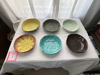Top-down photo showing all six pressed pottery bowls arranged on a white cloth surface with light filtering through curtains.