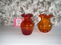 Two bright orange blown glass vases side by side on a pale background with a floral pattern.
