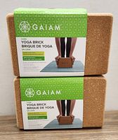 Photo of two stacked natural cork yoga bricks with green Gaiam branded labels describing them as cork yoga bricks.