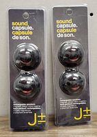 Front view of two JPM Sound Capsule rechargeable speaker packages, each containing two spherical black speakers in sealed packaging.