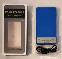 Photo of the Magic Speaker induction speaker in its plastic tray with USB power cable and packaging box visible.