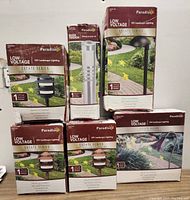 Photo showing boxed Paradise brand low voltage 12V landscape lighting fixtures from the Estate Series, including post lights and spotlights.