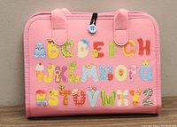 Front view of pink felt case with colorful alphabet letters in different patterns on the front surface.