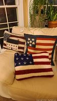 Three American flag themed pillows, including one crocheted, two with printed fabric, arranged on beige sofa.