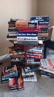 Photo of stacks of over 30 fiction books showing mostly Tom Clancy hardcovers and paperbacks along with other author's fiction books.